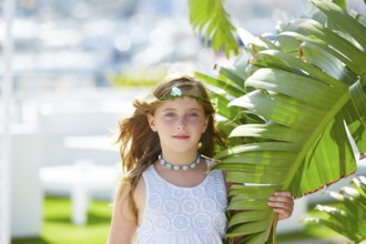 Blond kid girl at banana tree leaves in bright day light in Mediterranean