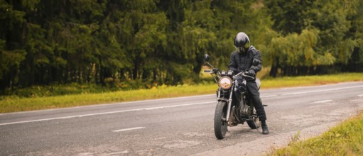A motorcyclist wearing a helmet on a road adjacent to a forest