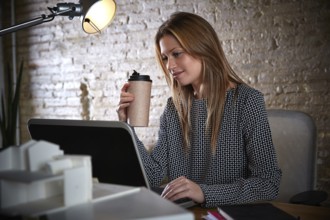 Businesswoman drinking coffee with laptop computer at office