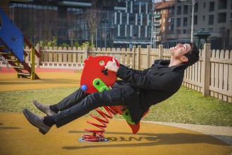 Young man reliving his childhood plying in a childrens playground riding on a colourful red spring