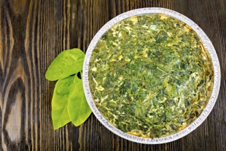 Celtic cake with spinach, tomatoes, oatmeal and eggs in baking dish from a foil, spinach leaves on