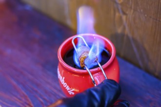 Red cup with burning sugar over mulled wine on a wooden bench, Straubing, Lower Bavaria