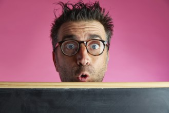 Nerd man crazy behind a blackboard funny surprise gesture in pink background