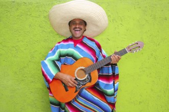 Mexican typical man playing guitar poncho on green wall