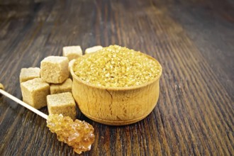 Granulated brown sugar in a bowl, crystalline on a stick and diced on a dark wooden board