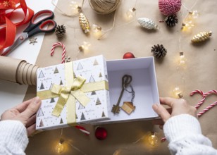 Key to house with keychain on cozy home in gift box with Christmas decor packaging. Pack present