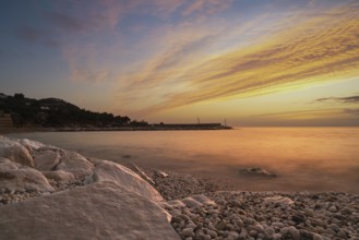 A colourful sunrise over the white pebble beach and harbor of Mattinata in Italy