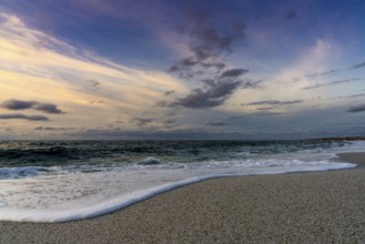 A low angle view of white sand beach with waves rolling in under a colorful sunset sky