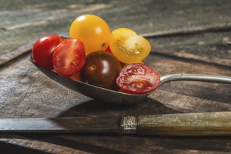 Variety of cherry tomatoes in spoon on wood