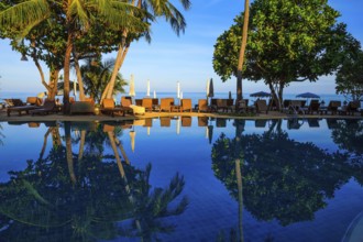 Sunset on the beach resort. An oceanfront pool surrounded by palm trees. Palm trees reflected in