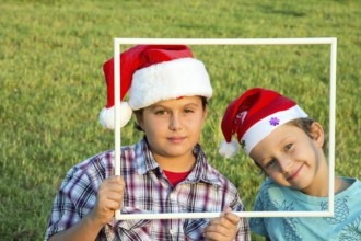 Two brothers in joke caps Santa Claus have fun smiling at the audience, holding a white frame.