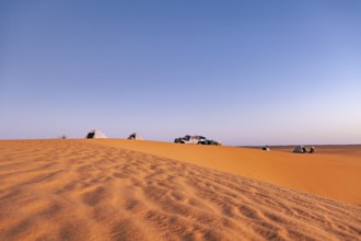 Tents and cars standing on a sand dune in the desert under a wide sky at sunset, camping in the