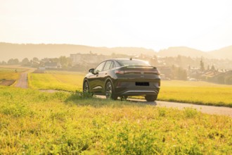 SUV driving on a country road with a view of a town at sunset, VW ID5 electric car, Calw, Black