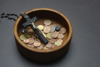 Crucifix with coins and buttons in a wooden bowl, church and money