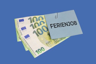 Holiday job symbol image: euro banknotes and a piece of paper with the words HOLIDAY JOB cut out