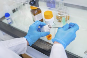 Person in a laboratory puts a small amount of powder into a beaker with a spatula, Youth Research