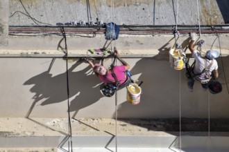 Painter hanging from a rope while working on a façade, symbolic image for safety in construction,