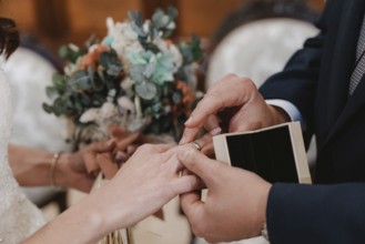 Close up of a couple exchanging rings during a wedding ceremony, with a beautiful bouquet in the