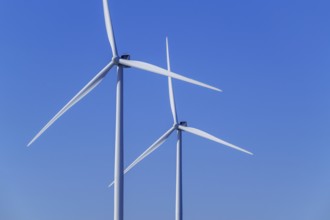 Two wind turbines showing tower, nacelle and huge rotor blades against blue sky