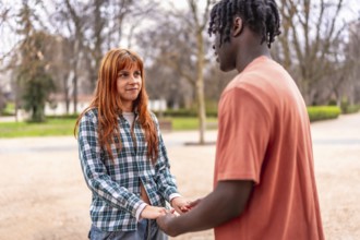 Interracial couple holding hands and talking in a park, enjoying a romantic moment together