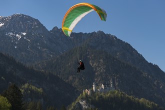 A paraglider flies near Neuschwanstein Castle in front of an impressive mountain landscape,