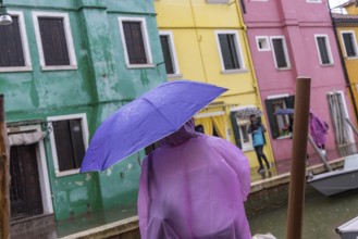 City view of Burano with colourfully painted houses and canals. Rainy weather, people are carrying