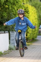 Boy practising to ride a unicycle, sidewalk, Germany