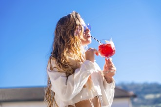 Sensual blonde woman drinking a cocktail in a rooftop facing the sun in summer