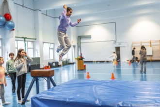 Schoolgirl practicing vaulting in a gym class, watched by her classmates and teacher, demonstrating
