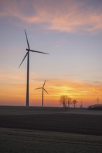 Three wind turbines in front of a beautiful sunset sky with trees, near Ulm, Swabian Alb,