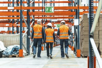 Warehouse workers wearing high visibility vests and hard hats are walking through a logistics