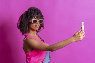 Fashionable young woman taking a selfie with smartphone, wearing sunglasses and pink top on a