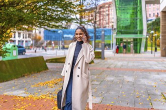 Happy african businesswoman talking to the mobile while walking along the city after work