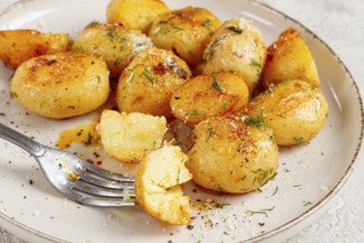 Half-eaten fried new potatoes, with butter and dill, on a white plate, with a fork, at home, no