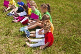 The good kids in colorful t-shirts sit on the grass with books in their hands