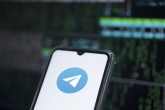 The TELEGRAM app logo on the screen of a cell phone that a man is holding.