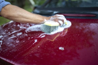 A person cleaning a red car with a sponge, creating soapy suds
