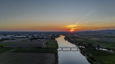 Wide river landscape with railway bridge in the middle, setting sunlight and extensive fields,