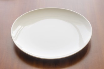 An empty white modern plate on a wooden table