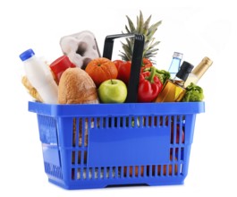 Plastic shopping basket with assorted grocery products isolated on white