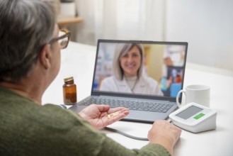 Senior woman having online medical consultation with doctor using laptop, holding pills in hand and