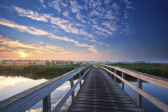 Wooden bridge over river at summer sunrise