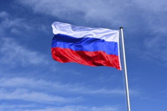 The flag of Russia flutters in the wind against a blue cloudless sky