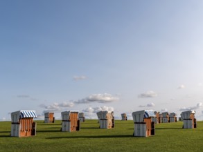 White beach chairs on a meadow and blue sky with clouds in the background, along the coast of the