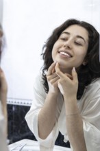 Portrait of a happy woman removing pimples and blackheads from her face in front of the mirror at