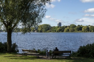 Leisure activities in summer, bicycle and woman on park bench, blue sky, Alster with Hotel