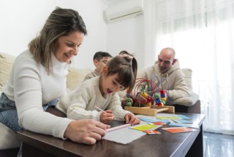 Mother helping daughter drawing while father and son playing with toys in the living room