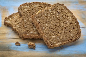 Slices of organic, whole grain, dark rye bread on painted wooden cutting board