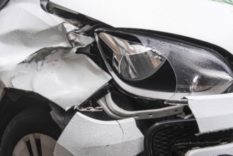 A heavily damaged white car after an accident. The front left mudguard is badly dented and