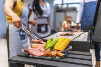 Chefs preparing a barbecue with meat, corn and vegetables on a glass tray, ready to be grilled